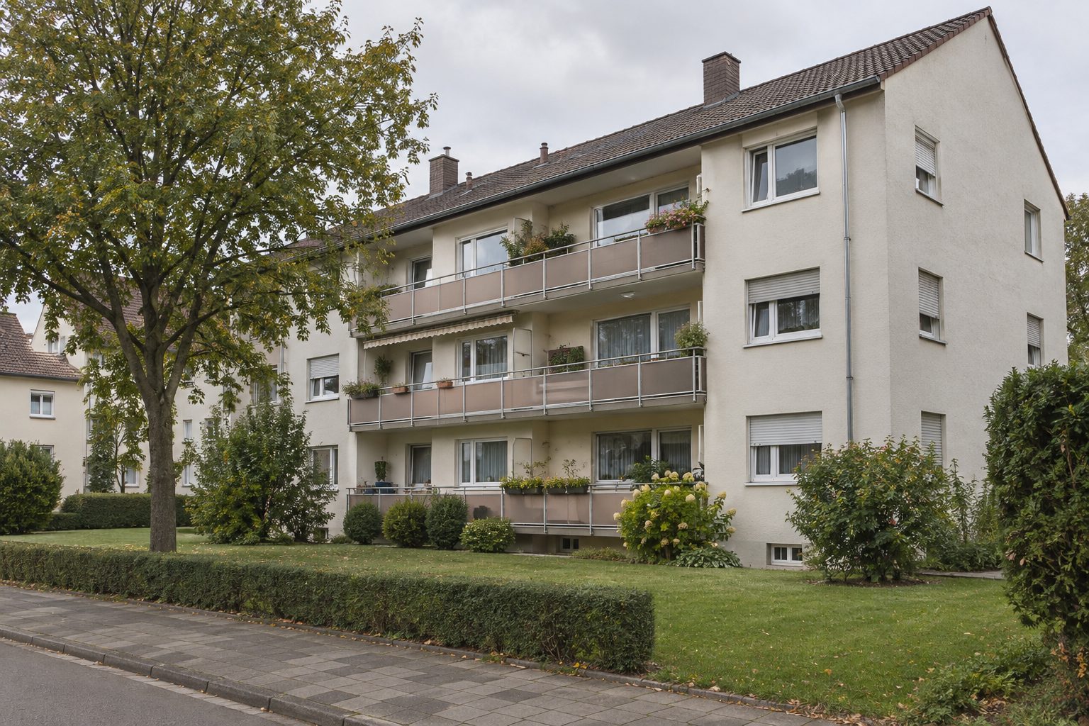 Mehrfamilienhaus aus der Nachkriegszeit mit durchgehenden Balkonen, Rasen und Hecke